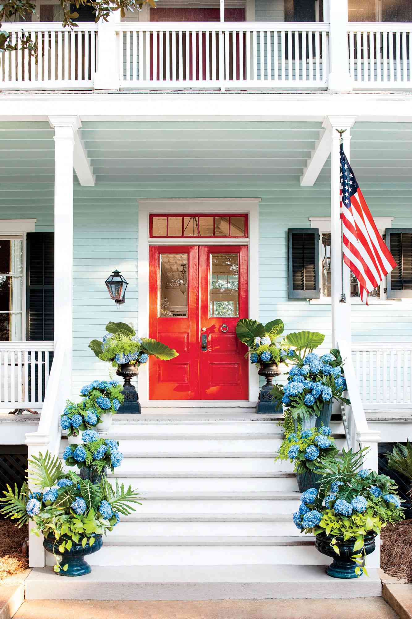 Strålende rød inngangsdør på et lyseblått hus med beholdere med hortensia