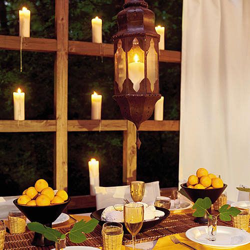 white candles are placed on the wooden ledges surrounding the deck with a table decorated with lemons in bowls, a hanging lantern, white plates and wine glasses