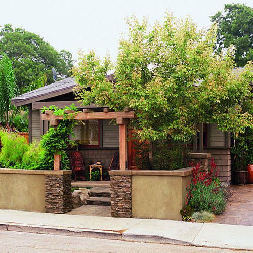 bungalow home with a large bush in front and a low wall around the front of the yard